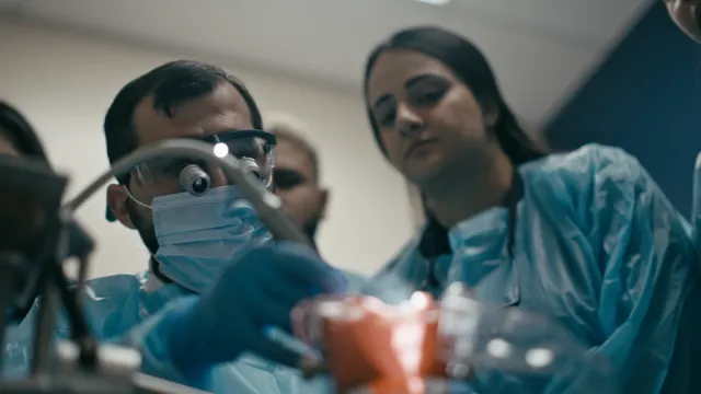 Close-up of a dentist and observing student performing a clinical procedure on a model with loupes.